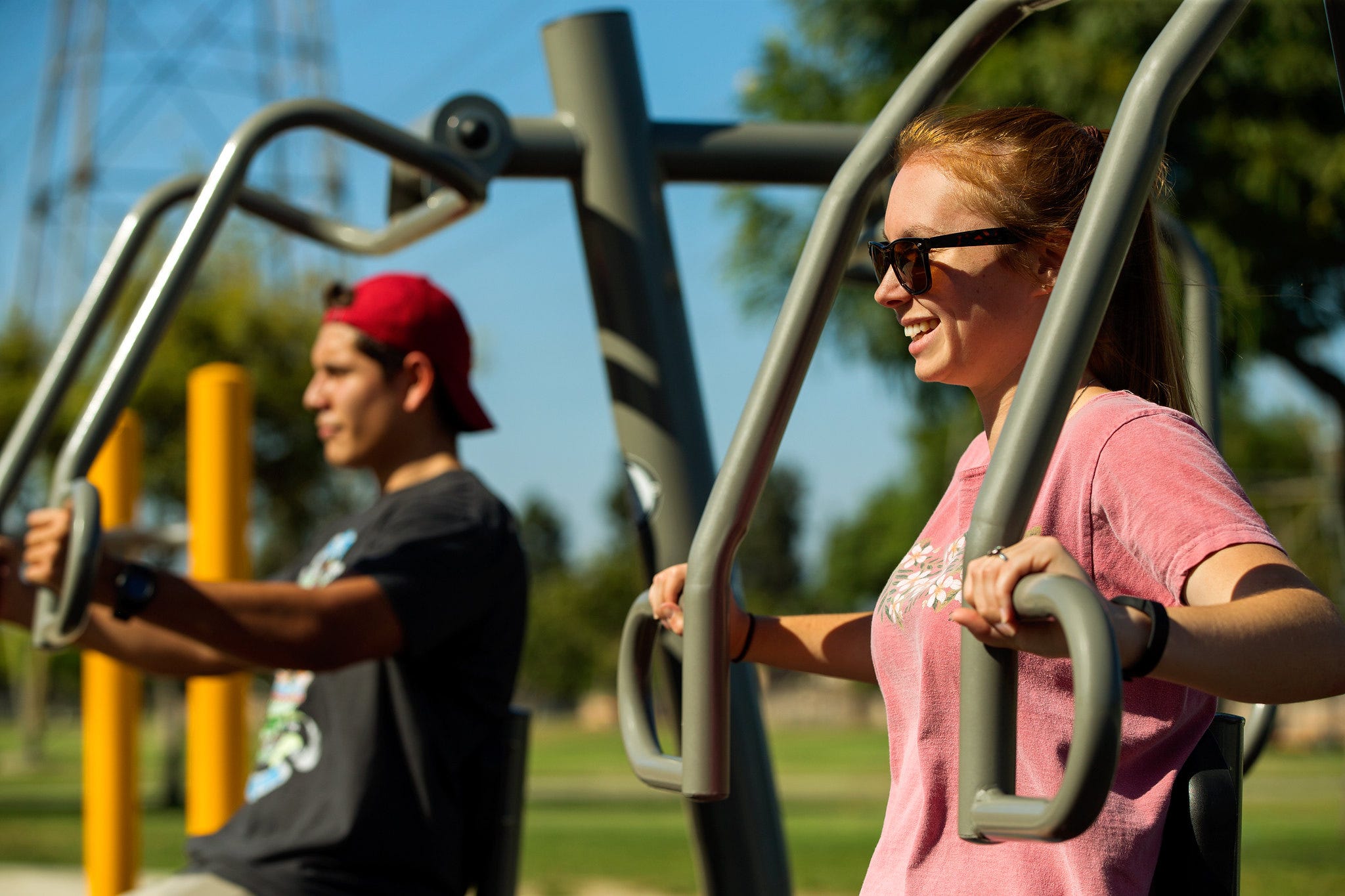 Woman and man using outdoor fitness equipment chest presses in a park